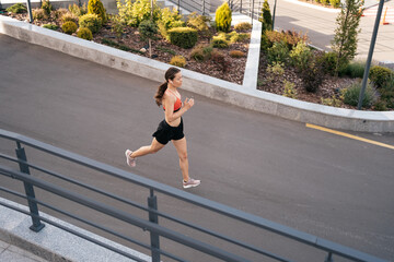 Young woman sprinting in the morning outdoors. Side view of female runner working out in the city.