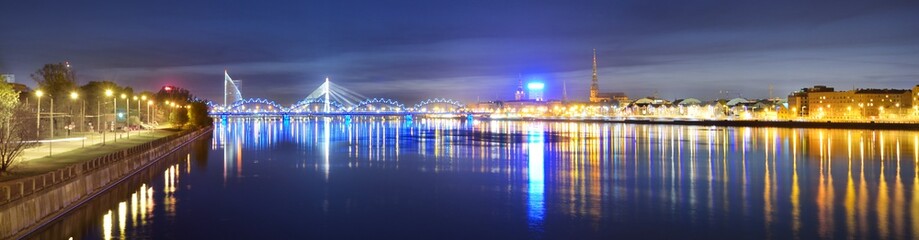 Panoramic view of the illuminated Old Town, cable-stayed and railway bridge in Riga at night....