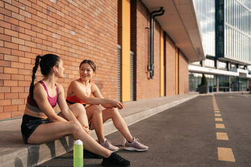 Two women before urban workout. Girls preparing for running and sitting in the street. Fitness break