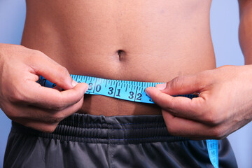 young man measuring his waist with a tape measure, close up.