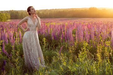 A full-length girl in a long evening dress in a field of lupines. Beautiful girl with hair and...