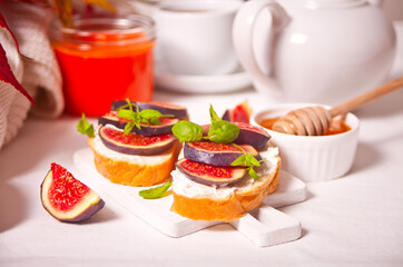 Sandwiches with cream cheese, figs and honey on the white board. Healthy breakfast food concept.