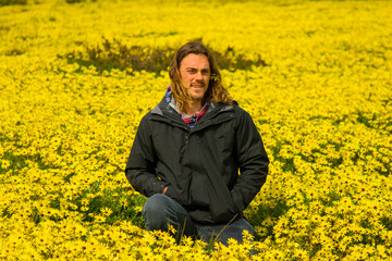 Field of yellow wild flowers with smiling young man