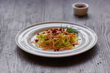Fresh cabbage salad made from shredded white cabbage, carrots and berries on a white plate. Top view, wooden background, selective focus