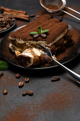 portion of Classic tiramisu dessert on ceramic plate on concrete background