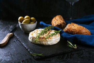 Camembert cheese with rosemary, olives and rustic bread on a dark background