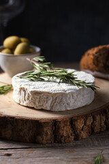 Camembert cheese with rosemary, olives and rustic bread on a wooden background