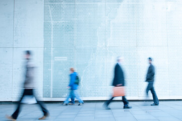 Motion blurred image of people walking against a light coloured wall