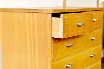 An old chest of drawers with shiny handles stands against a white wall.