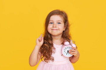 Time for a party. A pensive cute child in a fancy dress holds a small alarm clock in his hands and...