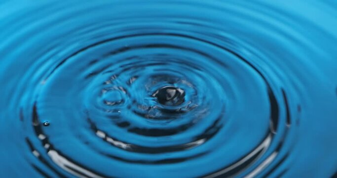 Zoom of a drops of water falling in blue water. Beautiful circular wave, ripple.