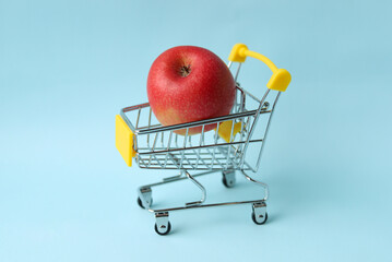 A ripe juicy red Apple in a shopping cart on a blue background. Selective focus.