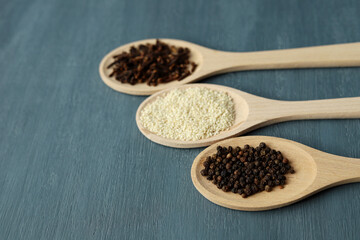 Three wooden spoons with spices lie on a wooden gray background. Selective focus. Various spices: cloves, black pepper and sesame.