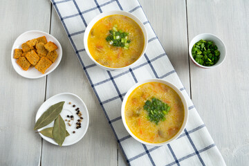 Noodle soup on a cotton napkin in two white bowls. Next to sliced green onions, crackers, spices. Delicious vegetarian food top view on white wooden background.