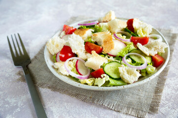 Lebanese salad fattoush. Healthy vegetarian food. Traditional lebanon salad with toasted pita bread and vegetables in the white plate on the canvas napkin with fork. Close up