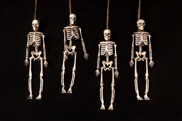 Four toy skeletons flat lay a dark background. Hanged with a rope around their necks. The symbol of...