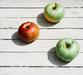 Fresh apples in the kitchen on the table, three apples. One red Apple and two green apples lie on a white wooden background.