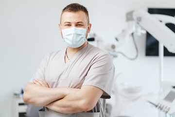 Fototapeta na wymiar Portrait of man dentist wearing medical mask with crossed arms in dental clinic