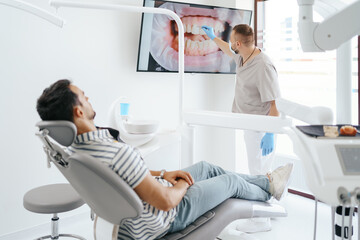 Dentist discussing with laying patient showing the image of his teeth on the screen