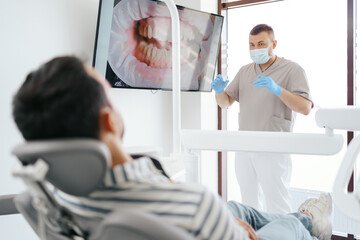 Naklejka premium Dentist discussing with laying patient showing the image of his teeth on the screen