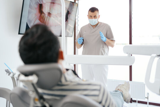 Dentist discussing with laying patient showing the image of his teeth on the screen