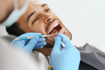 Smiling young man sitting in dentist chair while doctor examining his teeth