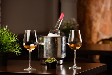 glasses with wine and olives, metallic ice bucket with bottle of wine inside, on the wooden table, inside the restaurant and free space for decoration.