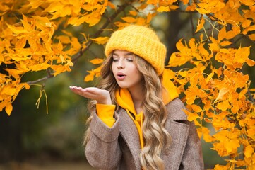 Beautiful girl walking outdoors in autumn. Smiling girl collects yellow leaves in autumn. Young woman enjoying autumn weather.