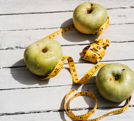 Food for a healthy lifestyle, delicious and healthy food, vitamins and minerals. Three green apples lie on a white wooden background and next to them is a yellow flexible meter-long ribbon.