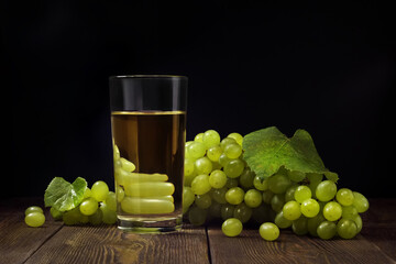 Bunch of sweet green grape and glass of fresh fruit juice on wooden table over dark background.
