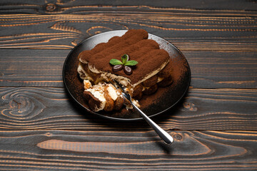 portion of Classic tiramisu dessert on ceramic plate on wooden background