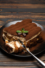 portion of Classic tiramisu dessert on ceramic plate on wooden background