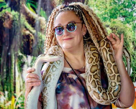 Pretty woman with curly hair with a live spotted python around her neck in Simply Butterflies Conservation Center on Bohol island, Philippines