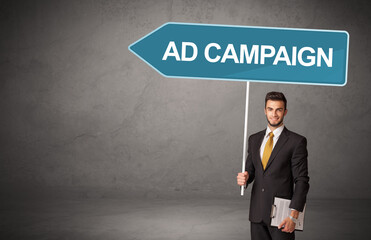 Young business person in casual holding road sign with AD CAMPAIGN inscription, new business direction concept