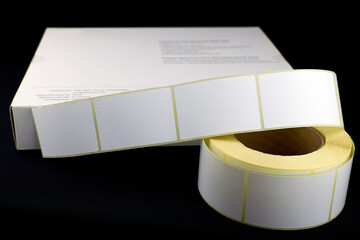 Roll of labels for thermal perforation on a white box.Stickers for thermal or thermal transfer printing. Cardboard box and Babina labels for printing on a black background.