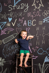 cheerful three-year-old boy on the background of a large blackboard with bright chalk drawings. black wall with children's drawings and formulas. vertical photography. look into the camera.
