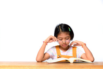 Asian female kid who wear glasses while concentrate reading a textbook on table on white background in studio. Learning of Schoolgirl. Memorize, learning by heart concept.