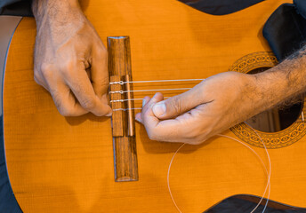 
Male hands changing the strings of a classical guitar
Luthier putting nylon strings on a Spanish...