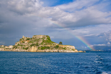 View of ancient venetian fortress on the hill at Corfu Island, Greece. Old stone walls, covered with green grass, sea bay, blue sky and rainbow