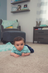 Little boy baby playing ins room on a carpet by his crib 