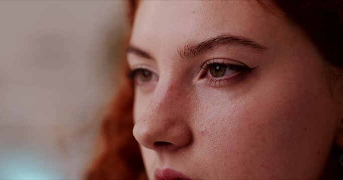 Side view close up of young red haired woman beautiful face with thoughtful worried facial expresion. Portrait of lady with penetrating look opening blinking eyes.