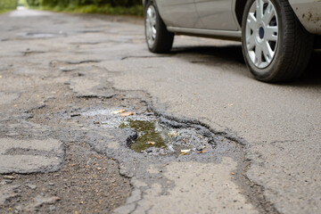 Modern silver car moving along the road with many potholes