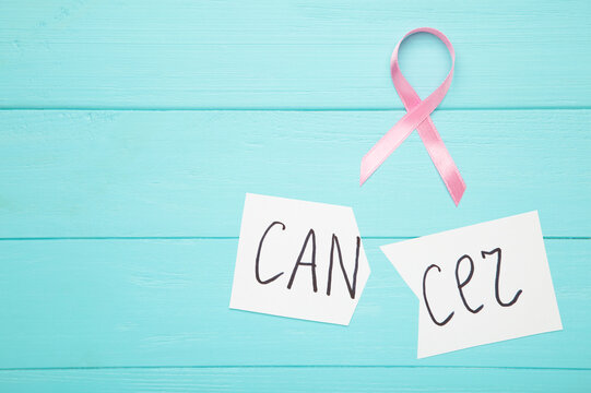 Scissors cutting a piece of paper with Cancer word with pink ribbon. Breast cancer awareness symbol.