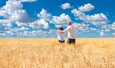 Naklejka na ściany i meble A young couple, a man and a woman in white shirts, run across a Golden wheat field, arms outstretched, miming flight. A man and a woman run into the field, rejoicing and enjoying life.