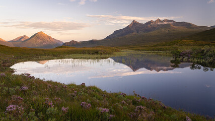 Panoramic view of Cuillin mountain range reflected in calm water of a small loch Nan Eilean on Isle of Skye, Scotland. Beautiful nature and landscape at sunset