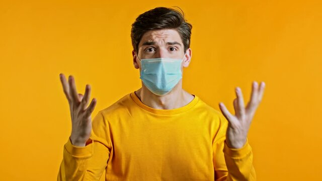 Angry irritated man in a protective mask screaming, asks when it will all end. Guy is tired of quarantine. Yellow studio background. Concept of pandemic, covid, corona virus