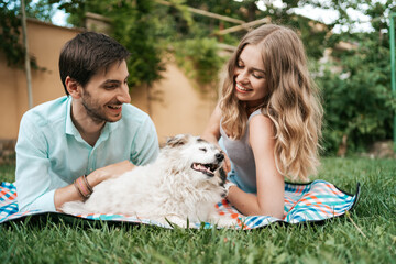 Happy couple of guys playing with their dog in the backyard on the grass. Cheerful old dog