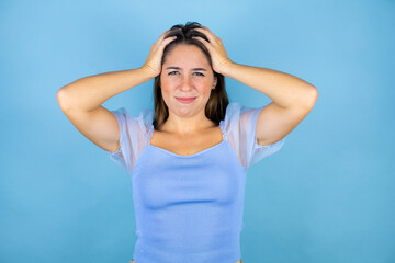 Young beautiful woman over isolated blue background crazy and scared with hands on head, afraid and surprised of shock