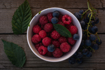 a bowl with raspberries and grapes, next to which lies a vine, surrounded by raspberry leaves