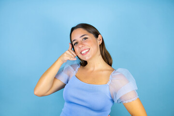 Naklejka premium Young beautiful woman over isolated blue background smiling doing phone gesture with hand and fingers like talking on the telephone